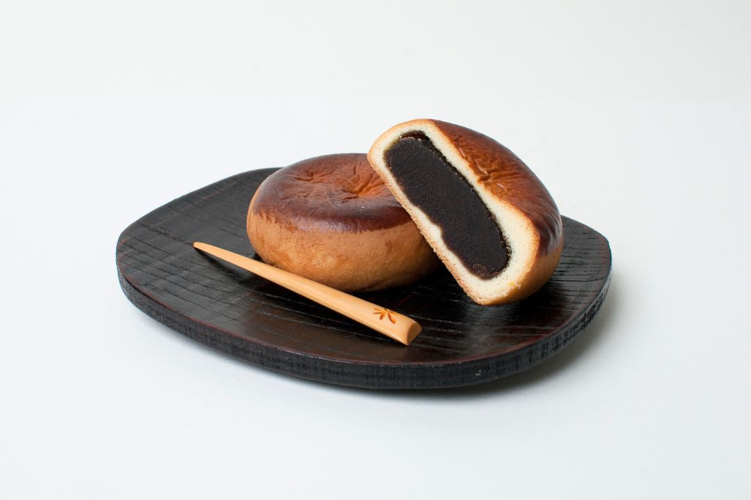 Wooden donut with black filling on a dark plate with a stick, on a white background